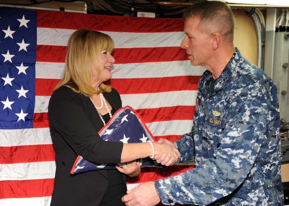 SAN DIEGO (Nov. 17, 2015) Cmdr. Theron Davis, commanding officer of the Los Angeles-class fast-attack submarine USS Hampton (767), presents a command coin to Cheryl Caleca, a Gold Star spouse whose husband passed away on active duty 40 years ago, on the mess decks of Hampton after a ceremony honoring Caleca's late husband's service. The Navy Gold Star Program assists family members of fallen service members in accessing benefits and resources to which they are entitled. (U.S. Navy photo by Mass Communication Specialist 3rd Class Derek A. Harkins/Released)