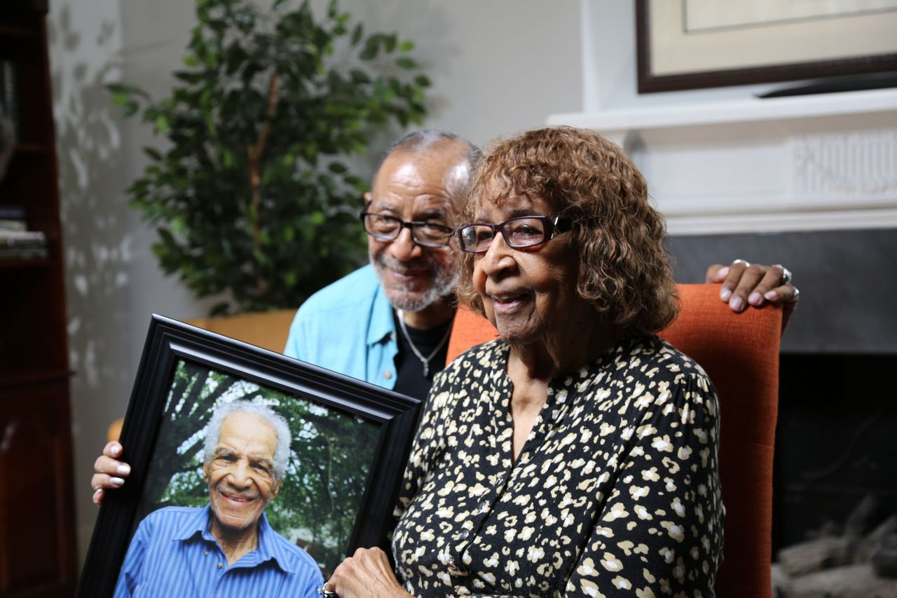 Vinnie and Beulah Dabney, son and wife of William Dabney, respectively, are pictured holding a framed portrait of Dabney Sr. while<br>at their home in Roanoke, Va. Corporal William Dabney served with the 320th Barrage Balloon Battalion on D-Day. (National Geographic/Shianne Brown)