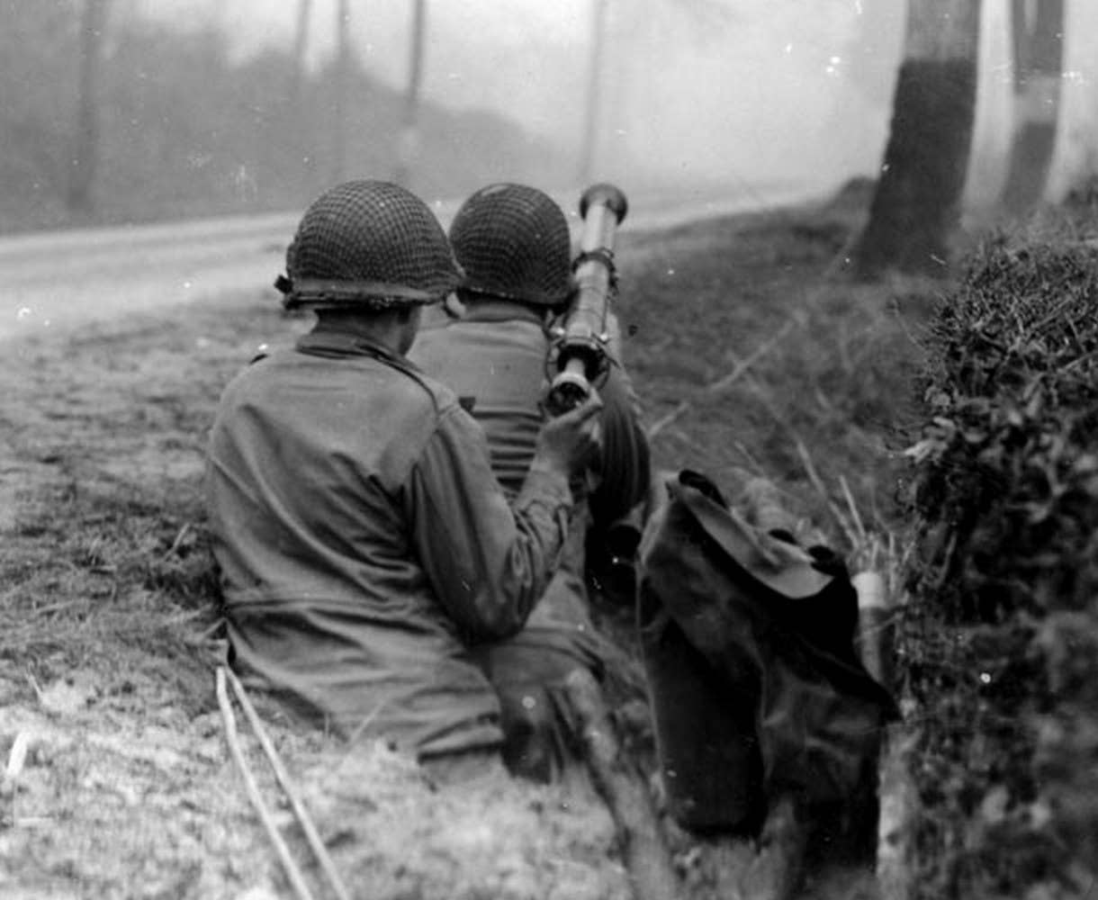 Two soldiers in the 82nd Airborne load and aim a bazooka at a German vehicle on road in France, 1944. (U.S. Army photo)