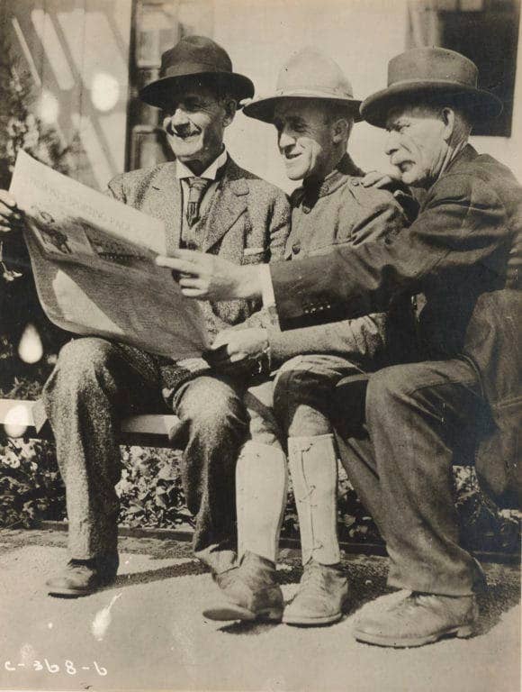 A father, son, and uncle share a newspaper on a visitor's day during training camp. (Photo: National Archives and Records Administration)