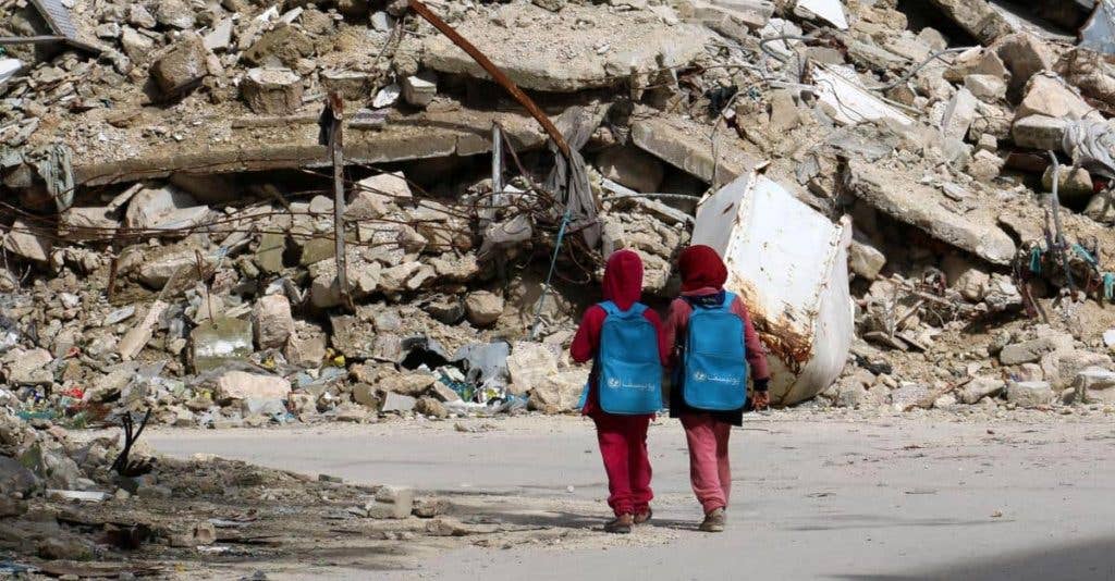 Syrian girls, carrying school bags provided by UNICEF, walk past the rubble of destroyed buildings on their way home from school on March 7 in al-Shaar neighborhood, in the rebel-held side of the northern Syrian city of Aleppo. (IZEIN ALRIFAI/AFP/GImages)