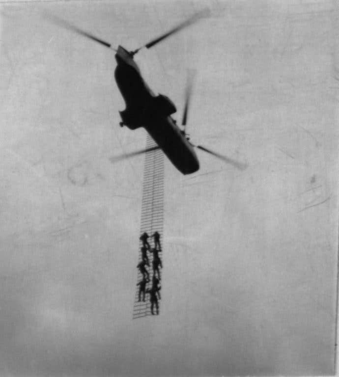 View of CH-46 helicopter passing over photographer as it carries nine ARVN Rangers hanging on an insertion ladder. The rangers are undergoing training in recon ladder insertion-extraction methods at first recon battalion area. (Photo: U.S. Marine Corps)