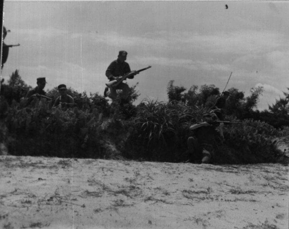 A Popular Force automatic rifleman and his assistant provide cover while a U.S. Marine advances and a Popular Force riflemen leaps over a row of cactus to pursue fleeing Viet Cong. The action occurred during a joint search and sweep operation near Chu Lai on Aug. 24, 1966. (Photo: U.S. Marine Corps Lance Cpl. Mincemoyer)