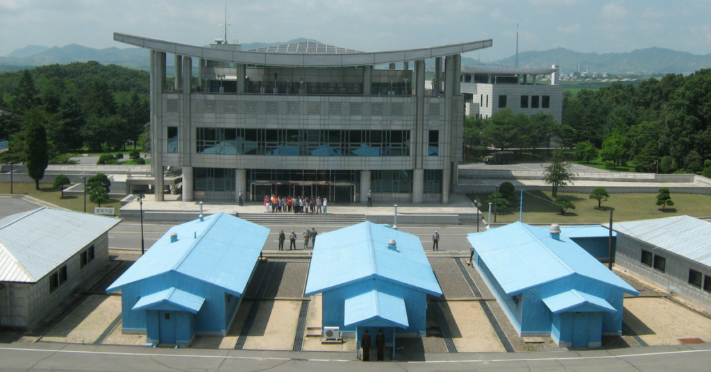 This shows the Conference Row in the Joint Security Area of the Korean Demilitarized Zone, looking into South Korea from North Korea. It shows guards on both sides and a group of tourists in the South. (Image Wikipedia)