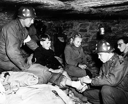 Captain Charles S. Quinn (right) of Louisville, Kentucky, bandages the gangrene-infected foot of Belgian refugee child in a cellar in Ottre, Belgium on Jan. 11, 1945. Captain Quinn was a battalion surgeon with the 83rd Division, First Army.