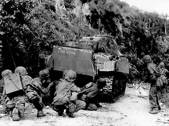 Marines take cover behind one of their medium tanks while cleaning out the northern north end of the island of Saipan on July 8, 1944. The Japanese were well dug in and making their last stand. (Photo: National Park Service)