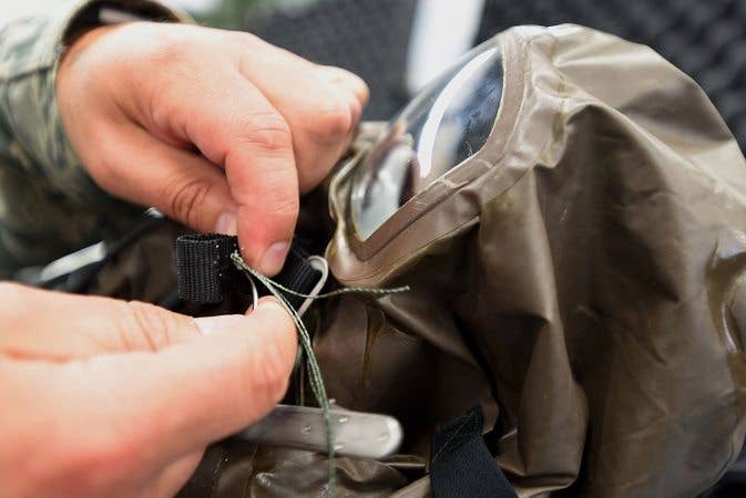 A soldier repairs clothing with a sewing kit, number 2 on our list of useful gear. 