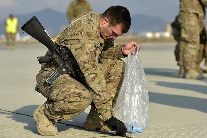 A soldier picks up FOD in a trash bag.