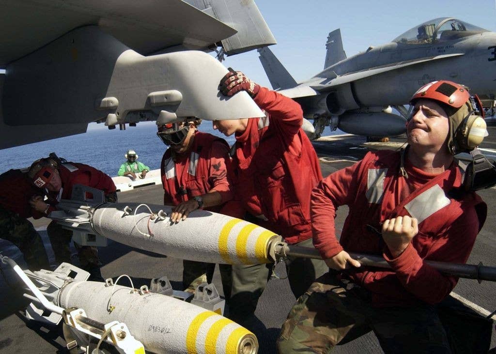 Ordies (in red jerseys) load 500-pounders onto Super Hornets aboard USS Abraham Lincoln (CVN 72). (Photo: U.S. Navy)