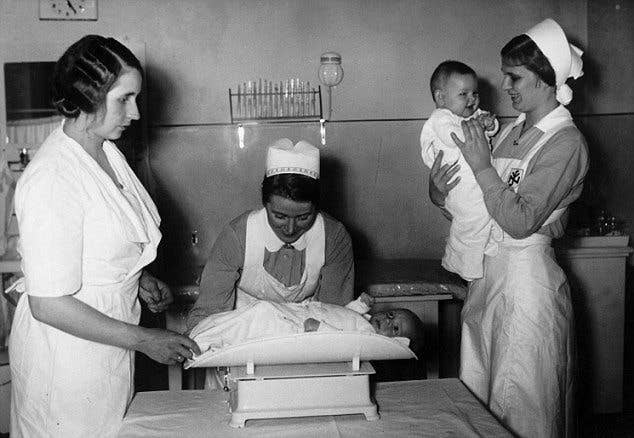 Two nurses weigh children at a Lebensborn house.