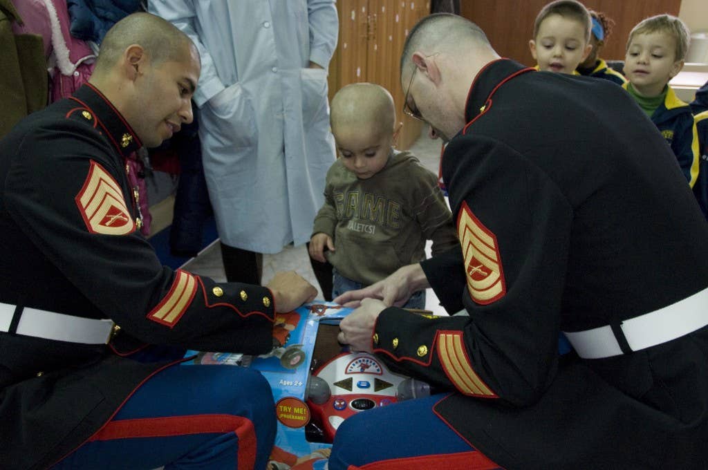 U.S. Marine Staff Sgt. Denis Licona, left, and Gunnery Sgt. Jarod Duke, help open a gift for a boy during a community relations event, at a school for underprivileged children. Marines and Sailors donated gifts to 60 children as part of the Marine Corps Toys for Tots Christmas Drive. (Photo by Daniela Muto |Released)