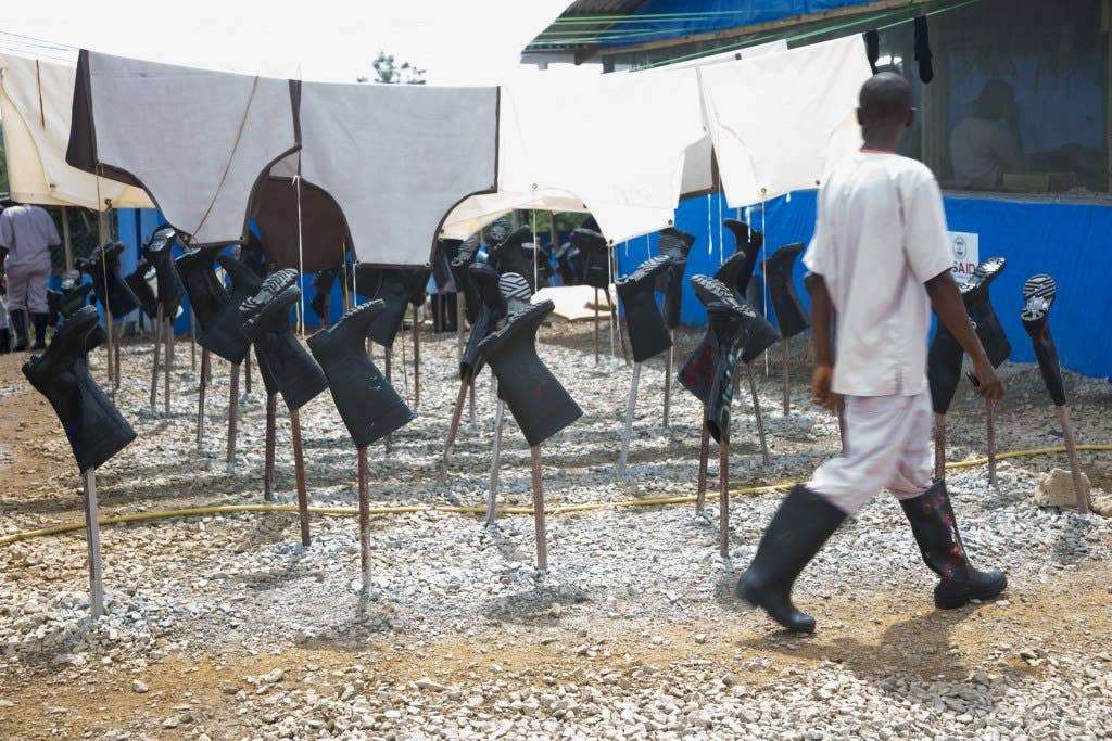 A local worker walks past rows of boots and aprons drying in the sun after being decontaminated at an active Ebola treatment unit built as part of Operation United Assistance in Suakoko, Liberia. United Assistance is a Department of Defense operation to provide command and control, logistics, training and engineering support to U.S. Agency for International Development-led efforts to contain the Ebola virus outbreak in West African nations. (U.S. Army Photo by Sgt. 1st Class Brien Vorhees)