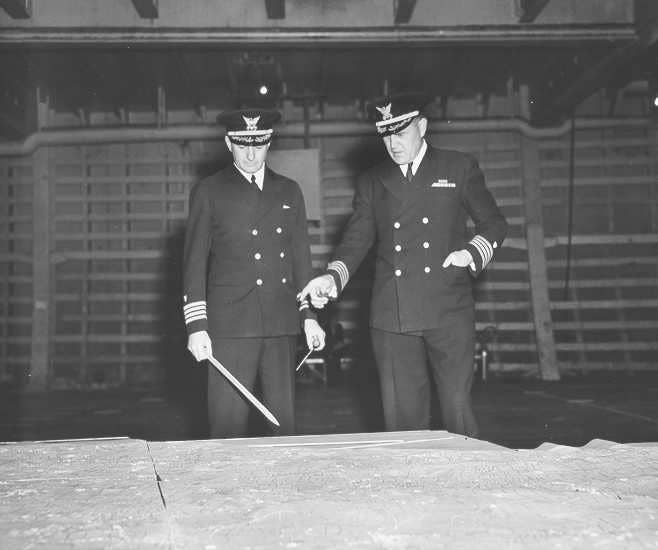 Coast Guard Captains Edward Fritzche (left) and Miles Imlay (right) discuss the invasion of Omaha Beach on a relief map laid out in the hold of the Samuel Chase. (U.S. Coast Guard photo)