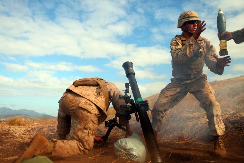 Lance Cpl. Kyle J. Palmer (left), holds a mortar tube steady as Lance Cpl. Samuel E. Robertson (right), mortarmen with the 81mm Mortars Platoon, Weapons Company, Battalion Landing Team 2nd Battalion, 7th Marines, 31st Marine Expeditionary Unit, grabs another mortar round during a joint live fire exercise, July 14. | Photo by U.S. Marine Corps