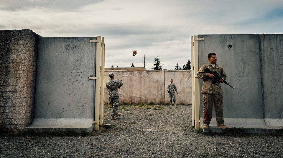 Two soldiers play catch with a football while a fellow soldier watches the perimeter of the training grounds during the Expert Field Medic Badge course at Joint Base Lewis-McChord, Wash., Sept. 24, 2015. The EFMB is the non-combat equivalent of the Combat Medical Badge and is awarded to medical personnel of the U.S. military who successfully complete a set of qualification tests. (U.S. Air Force photo by by Senior Airman Jordan A. Castelan)