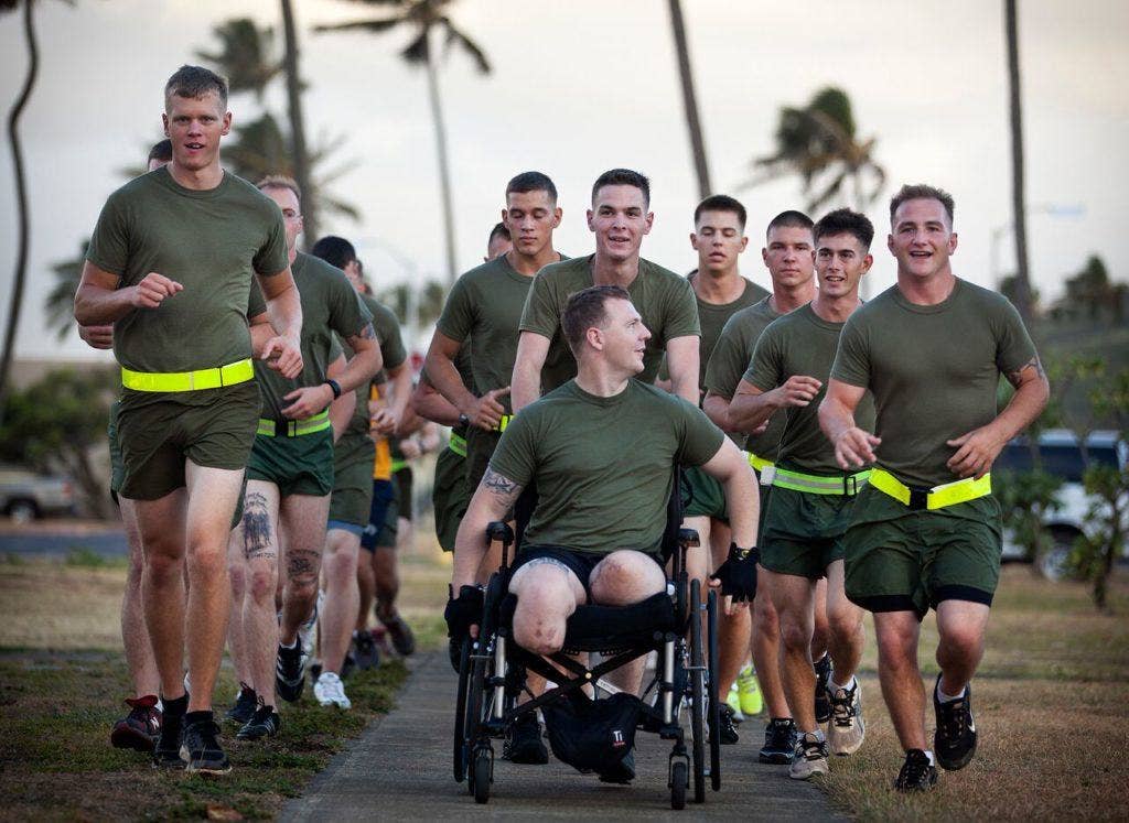 Cpl. Garrett Carnes (in wheelchair), a squad leader with India Company, 3rd Battalion, 3rd Marine Regiment, jokes with Sgt. Kenney Clark (right), a fellow India Co. squad leader, during a motivational run on Marine Corps Base Hawaii in Kaneohe Bay, Hawaii, May 29, 2012. Carnes lost his legs in an improvised explosive device attack Feb. 19, 2012 while supporting combat operations. (U.S. Marine Corps photo by Cpl. Reece Lodder)