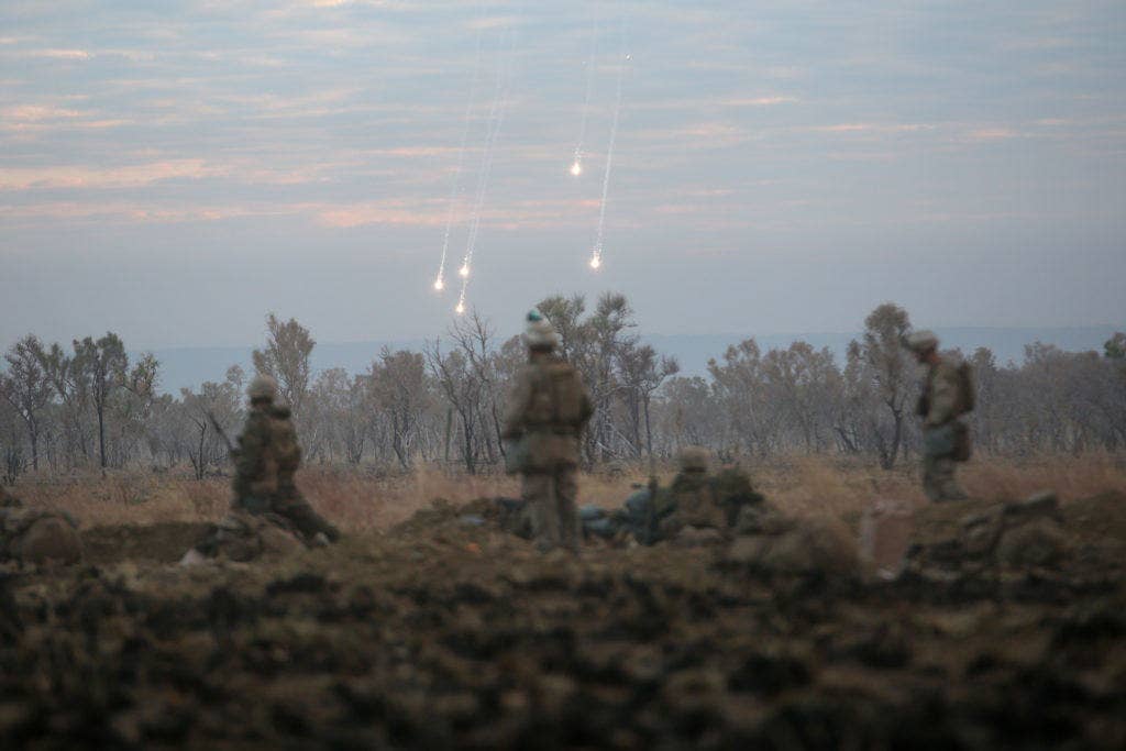 Marines with 1st Battalion, 1st Marine Regiment, watch illumination from artillery fall to the ground during a live fire range August 18, 2016, at Bradshaw Field Training Area, Northern Territory, Australia. The range was the final training evolution of Exercise Koolendong 16, a trilateral exercise between the U.S. Marine Corps, Australian Defence Force and French Armed Forces New Caledonia. Marines held a defensive position while engaging targets and working through the CS gas, which simulated a chemical attack. (U.S. Marine Corps photo by Sgt. Sarah Anderson)