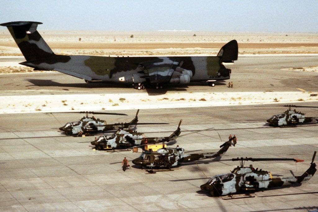 US Marine Corps Bell AH-1 Sea Cobra helicopters and a Bell UH-1N Twin Huey helicopter are parked on the flight line as a US Air Force C-5A Galaxy aircraft stands by after unloading supplies during Operation Desert Shield on January 23, 1991. | US Army