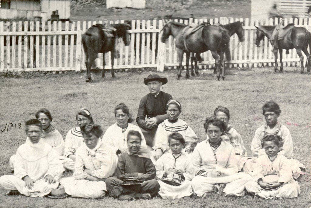 Father Damien, seen here with a girls choir, was canonized as a saint himself in 2009.