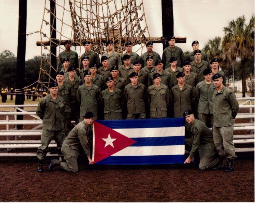 1st Platoon, B Co, 1st Ranger Battalion with a flag from Cuban barracks captured during the invasion of Grenada, 1983. (Photo by Bryan Staggs, who captured the flag and is standing in the front row, right)