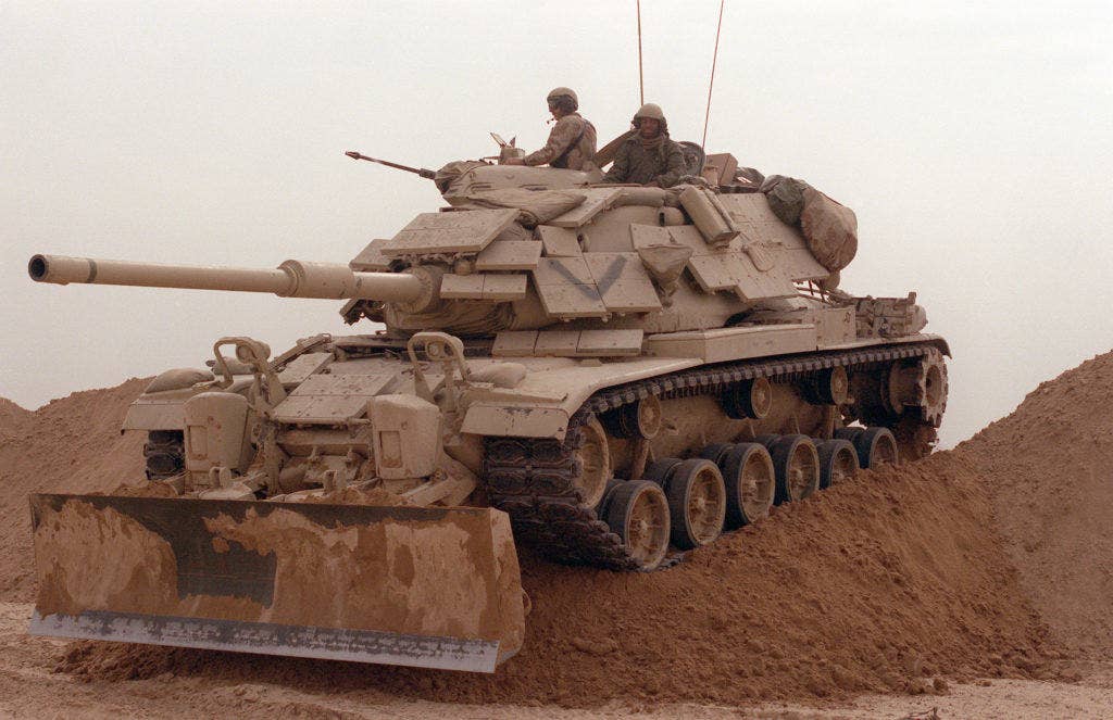 Marines from Company D, 2nd Tank Battalion, drive their M-60A1 main battle tank over a sand berm on Hill 231 while rehearsing their role as part of Task Force Breach Alpha during Operation Desert Storm. The tank is fitted with reactive armor and an M-9 bulldozer kit. (Photo: U.S. Department of Defense)