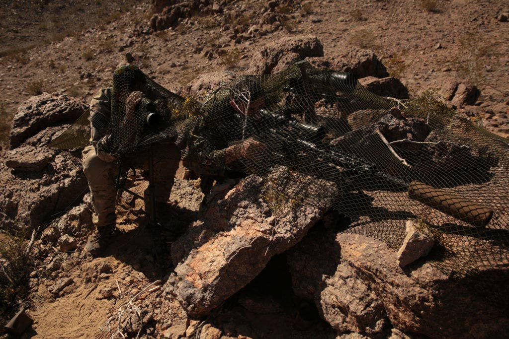 An Army Special Forces communications sergeant, 10th Special Forces Group (Airborne), spots targets and calls adjustments for his shooter on a mountainside.