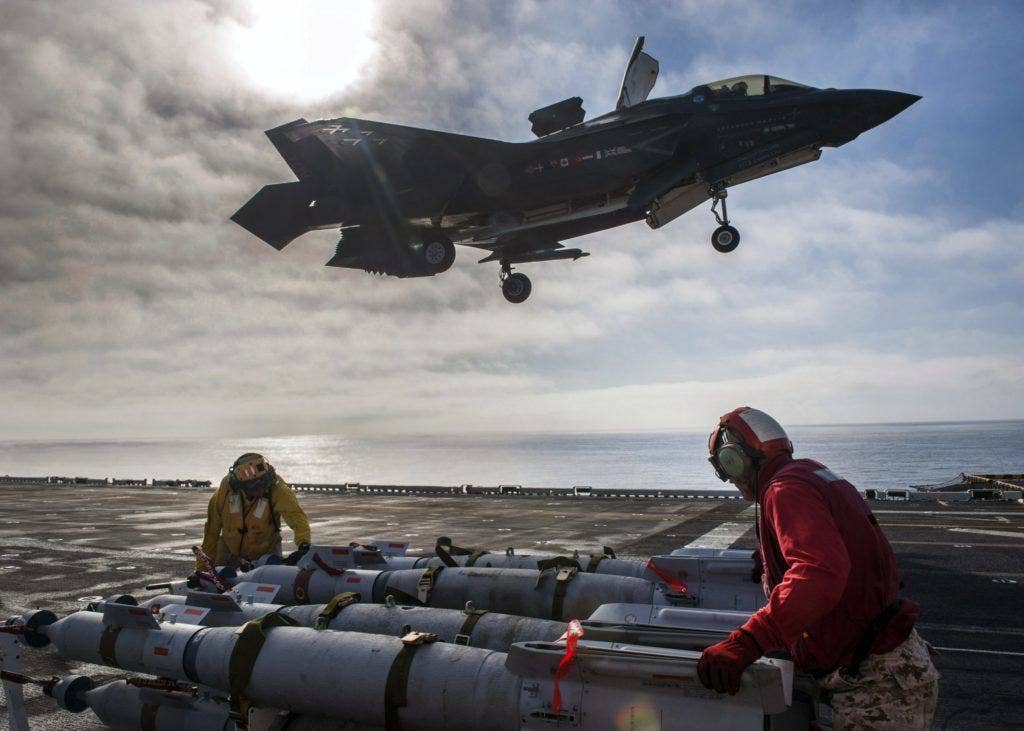 Sailors assigned to the amphibious assault ship USS America and F-35B Lightning II Marine Corps personnel prepare to equip the aircraft with inert 500-pound GBU-12 Paveway II laser-guided test bombs during flight operations. US Navy