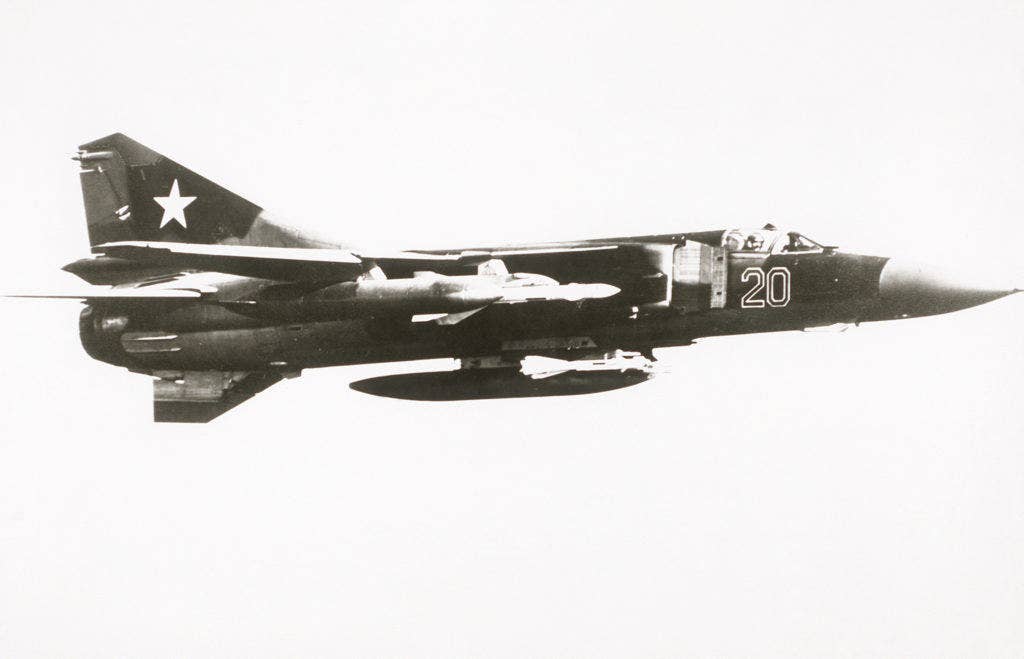 An air-to-air right side view of a Soviet MiG-23 Flogger-G aircraft with an AA-7 Apex air-to-air missile attached to the outer wing pylon and an AA-8 Aphid air-to-air missile on the inner wing pylon. (From Soviet Military Power 1985)