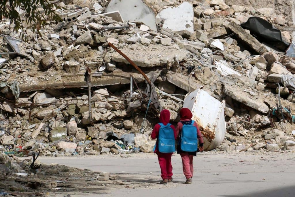 Syrian girls, carrying school bags provided by UNICEF, walk past the rubble of destroyed buildings on their way home from school on March 7 in al-Shaar neighborhood, in the rebel-held side of the northern Syrian city of Aleppo. (IZEIN ALRIFAI/AFP/GImages)