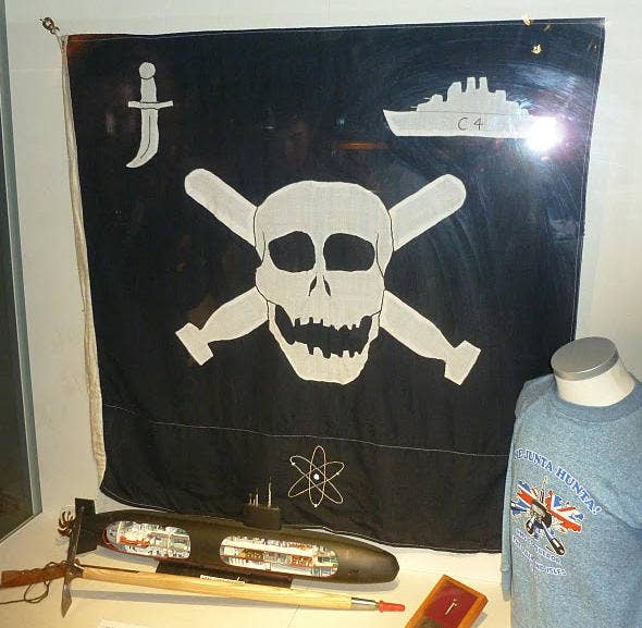 The Conqueror's Jolly Roger, featuring an atom for being the only nuclear sub with a kill, crossed torpedoes for the torpedo kill, a dagger indicating a cloak-and-dagger operation, and the outline of a cruiser for what kind of ship was sunk. (Royal Navy Submarine Museum)
