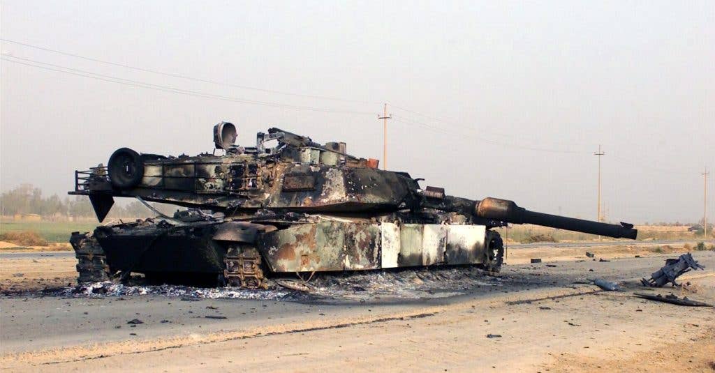 A scuttled M1A1 Abrams Main Battle Tank rests in front of a Fedayeen camp just outside of Jaman Al Juburi, Iraq, during Operation Iraqi Freedom. (Photo: Department of Defense)