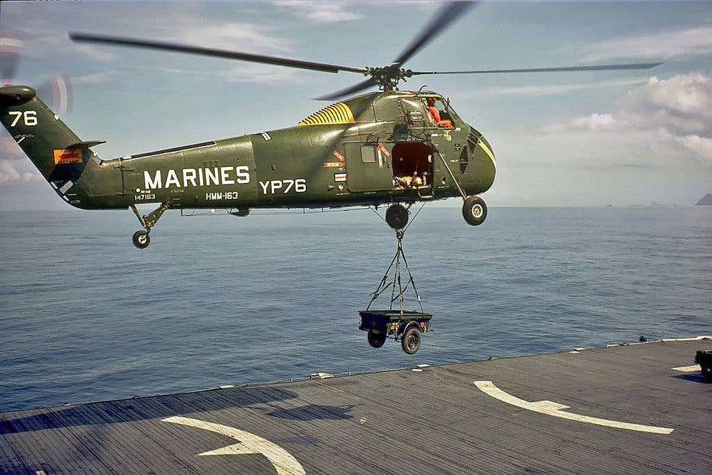 A Marine Corps UH-34 from Marine Heavy Helicopter Squadron 163 lifts a trailer off the deck of an amphib. (Photo via Wikimedia Commons)
