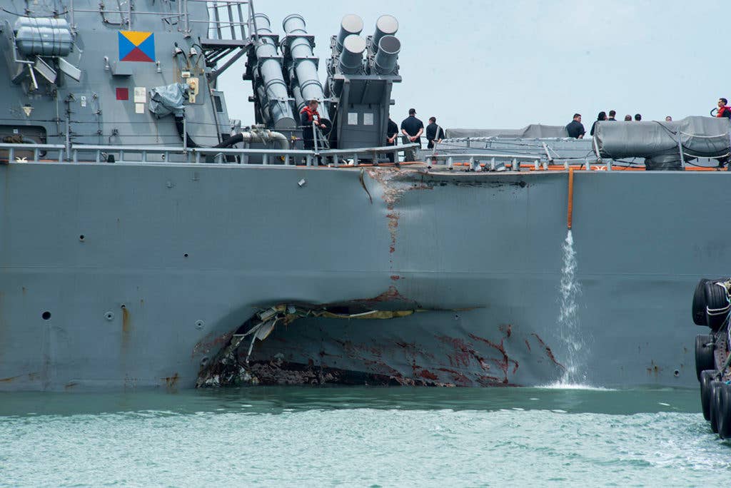 Damage to the portside is visible as the Guided-missile destroyer USS John S. McCain (DDG 56) steers towards Changi Naval Base, Republic of Singapore, following a collision with the merchant vessel Alnic MC while underway east of the Straits of Malacca and Singapore on Aug. 21. Significant damage to the hull resulted in flooding to nearby compartments, including crew berthing, machinery, and communications rooms. Damage control efforts by the crew halted further flooding. The incident will be investigated. (U.S. Navy photo by Mass Communication Specialist 2nd Class Joshua Fulton/Released)