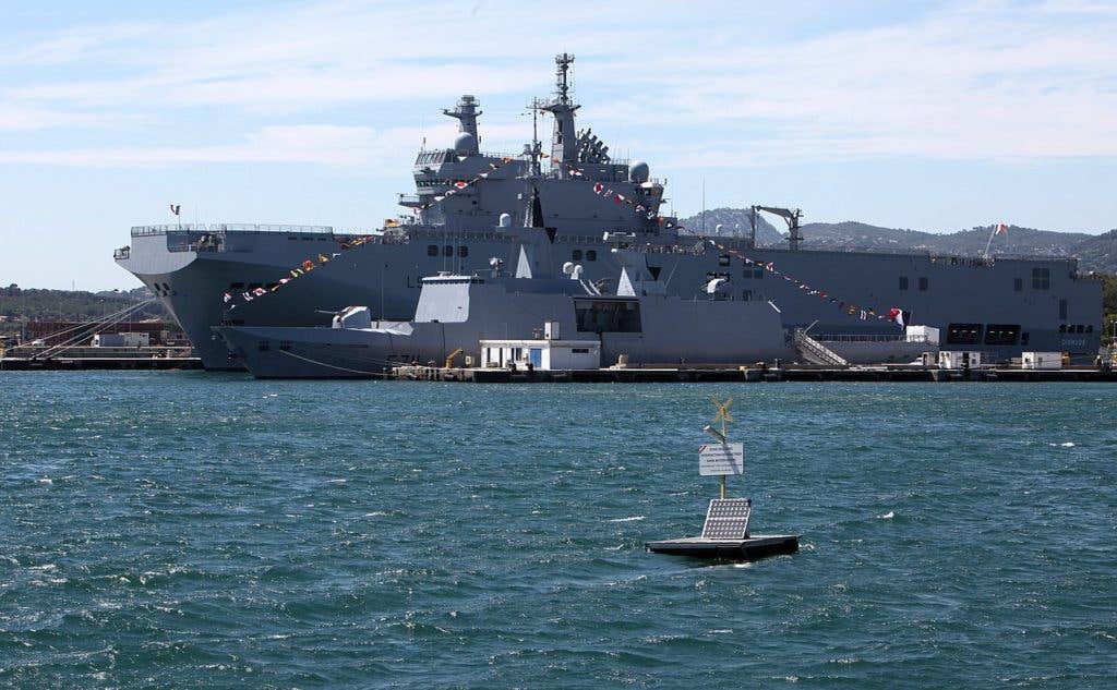 The BPC Dixmude (L9015) moored behind the LaFayette-class stealth frigate Surcouf (F711) on the 14th of July 2011, one day after she arrived in Toulon from Saint-Nazaire for fitting out. (Wikimedia Commons)