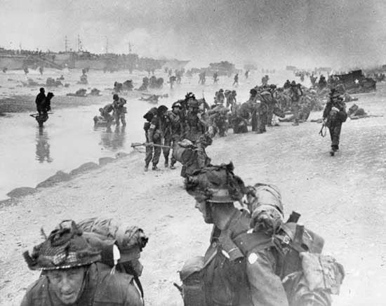 Injured and exhausted assault troops are helped ashore at Sword Beach on D-Day,