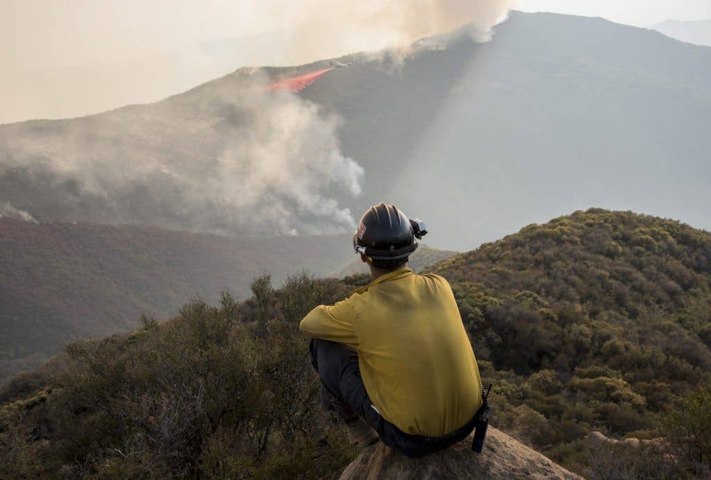 Tanner Renz, Kern County Fire Department, looks on as a C-130J Hercules from the 146th Airlift Wing, California Air National Guard, sprays fire retardant ahead of the leading edge of the Thomas Fire, Dec. 13, 2017. The 146th was activated to support CAL FIRE with wildfire suppression efforts within the state. The C-130s from Channel Islands Air National Guard Station are capable of spraying fire retardant from a modular airborne firefighting systems loaded in the cargo bay. (U.S. Air Force photo by Master Sgt. Brian Ferguson)