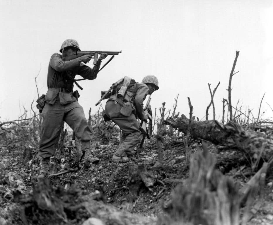 A Marine of the 1st Marine Division draws a bead on a Japanese sniper with his Tommy gun as his companion ducks for cover. The division is working to take Wana Ridge before the town of Shuri. Okinawa, 1945. (USMC photo)