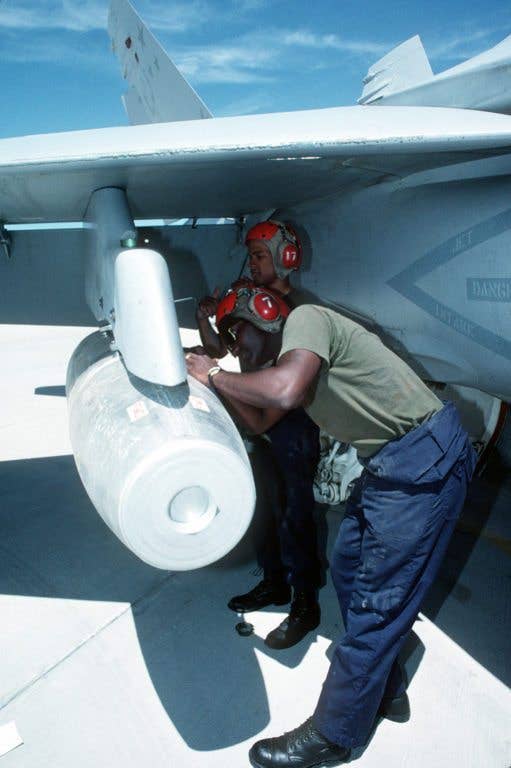 Sgt. Jamal G. Walker and Lance Cpl. Carl Feaster tighten the sway braces on a Mark 77 napalm bomb while loading it onto the wing pylon of a Marine Strike Fighter Squadron 321 (VMHA-321) F/A-18A Hornet aircraft. The Mark 77 is the modern version of the napalm bomb. (US Navy photo)
