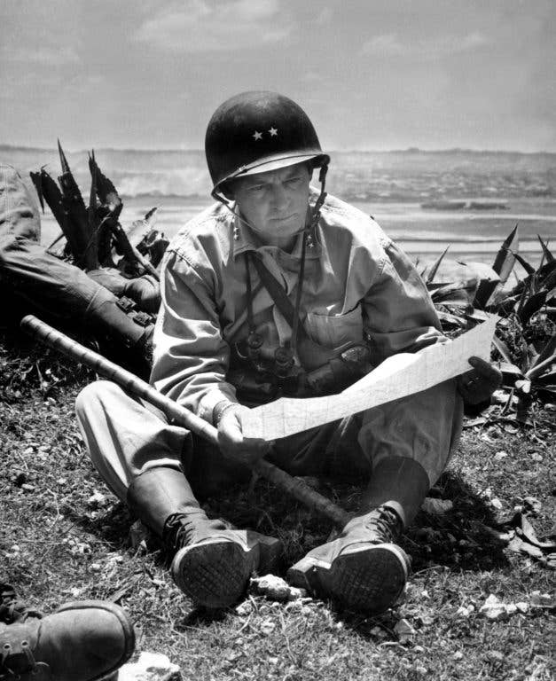 With the captured capital of Naha in the background, Marine Maj. Gen. Lemuel Shepherd, commanding general of the 6th Marine Division, relaxes on an Okinawan ridge long enough to consult a map of the terrain. (Marine Corps)