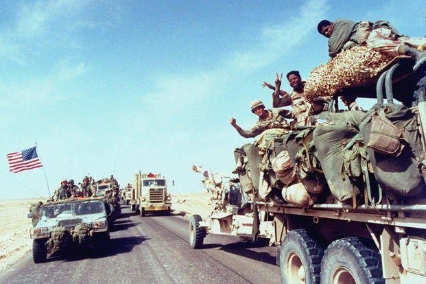 During Operation Desert Storm, American soldiers wave to the camera from a truck as their convoy moves into Iraq. (Photo by DOD)