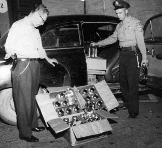 Police cleaning out the contents of a bootlegger's stock car.