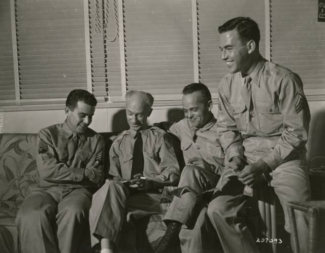 Ernie Pyle, preparing to cover the Pacific war front, gets a preview from enlisted men who have returned from the front. From left to right u2013 T/4 Al Levy (of Albany, NY), T/5 William Gharrity (of Chippewa Falls, WI), and Ssgt. Richard W. Bridenbaugh (of Toledo, OH)/ Date: January 1945.