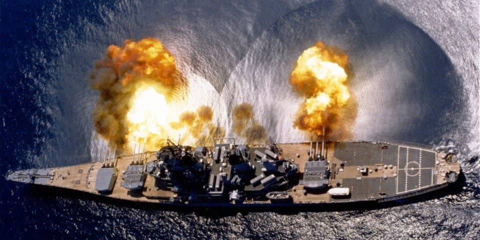 A WWII-era US battleship fires its deck guns.