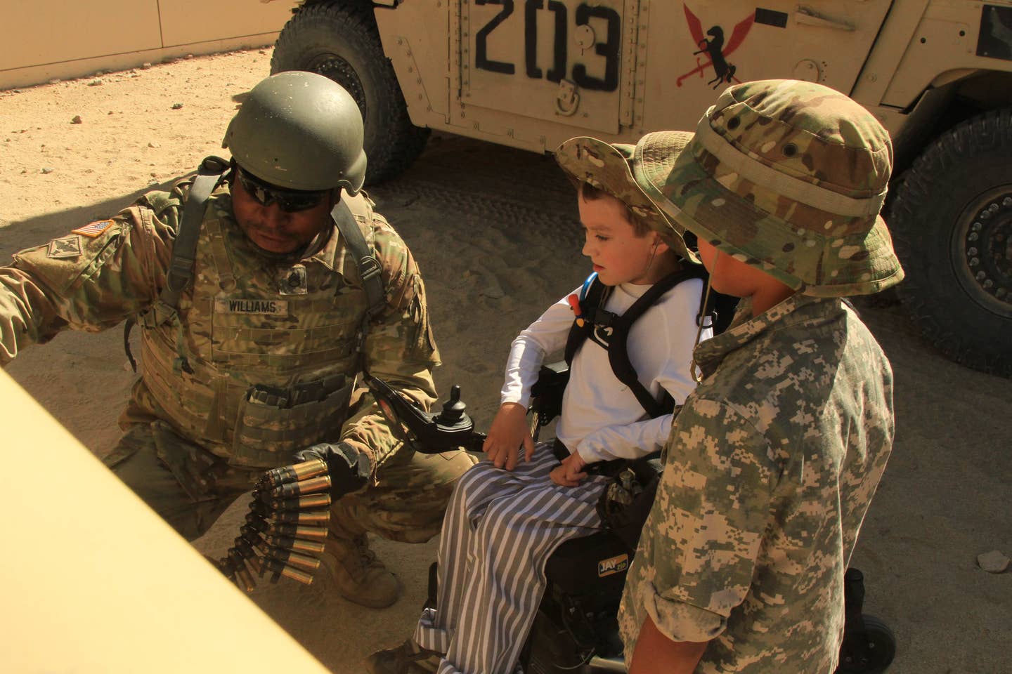Ethan Larimer, center, 11th Armored Cavalry Regiment Honorary Blackhorse Trooper, and Grant Averill, Ethan's friend, are briefed about the capabilities of the vehicle mounted Browning M2 .50 Cal. Machine Gun.