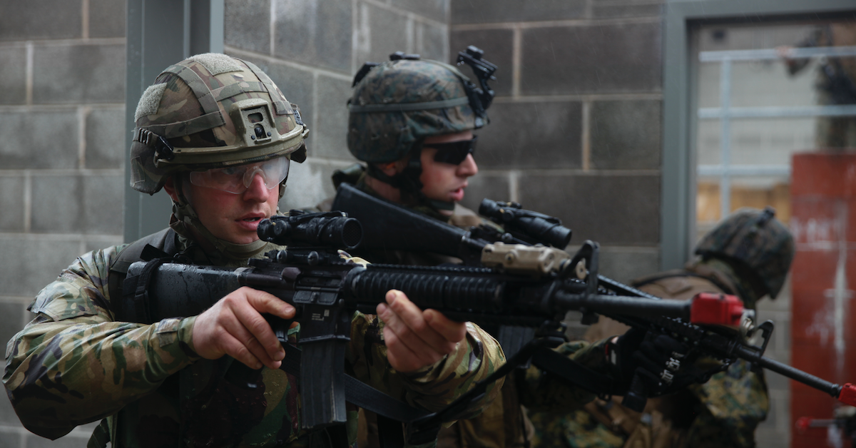 Two Marines hold their M164As and stand outside a cement building