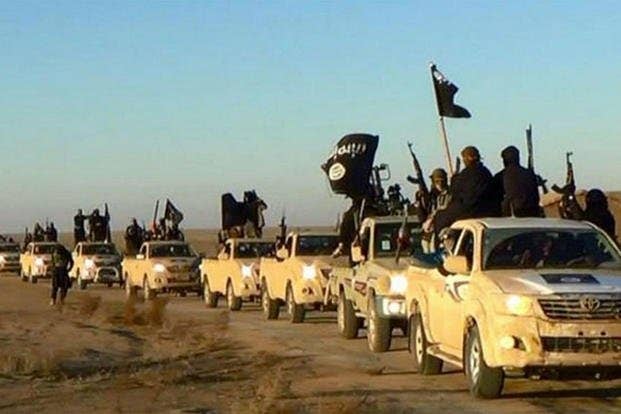 Militants of the Islamic State group hold up their weapons and wave its flags in a convoy.