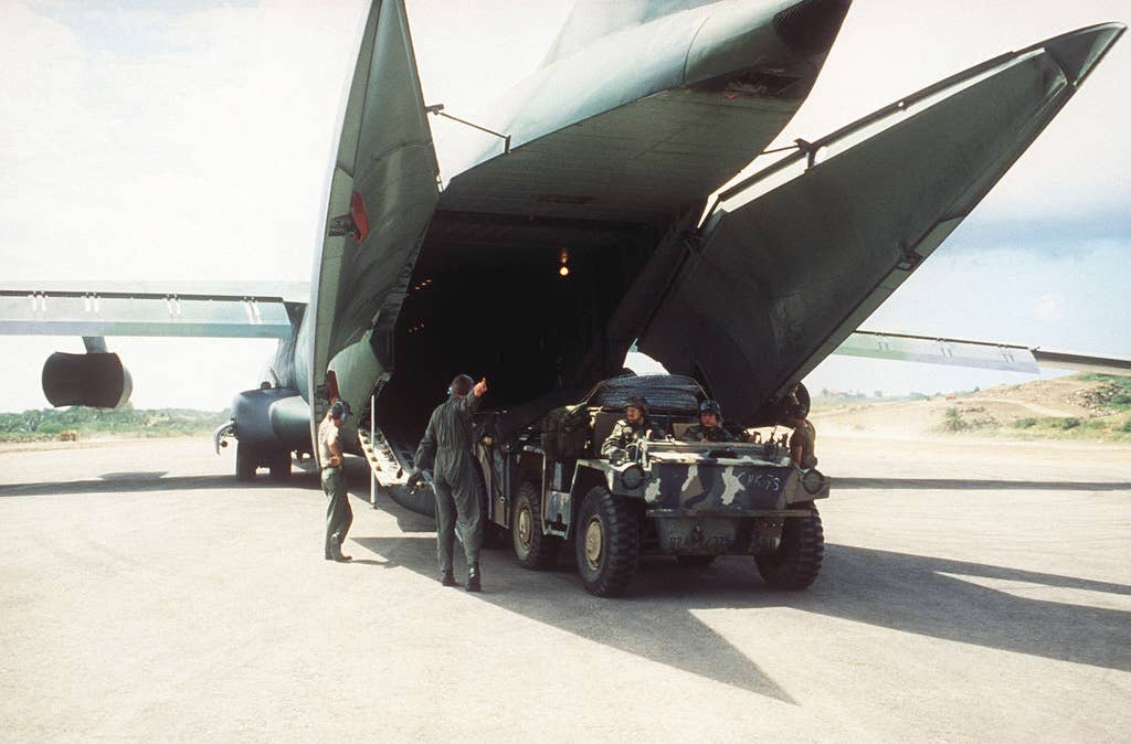 An M561 Gama Goat truck loaded with supplies prepares to pull away from a C-141B Starlifter aircraft parked on the flight line at Point Salines Airport during Operation Urgent Fury after the airfield was captured by Rangers. (Spc. Douglas Ide)
