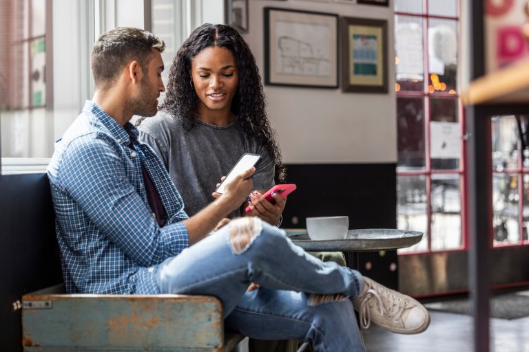Young couple using smartphones to transfer money in coffeeshop