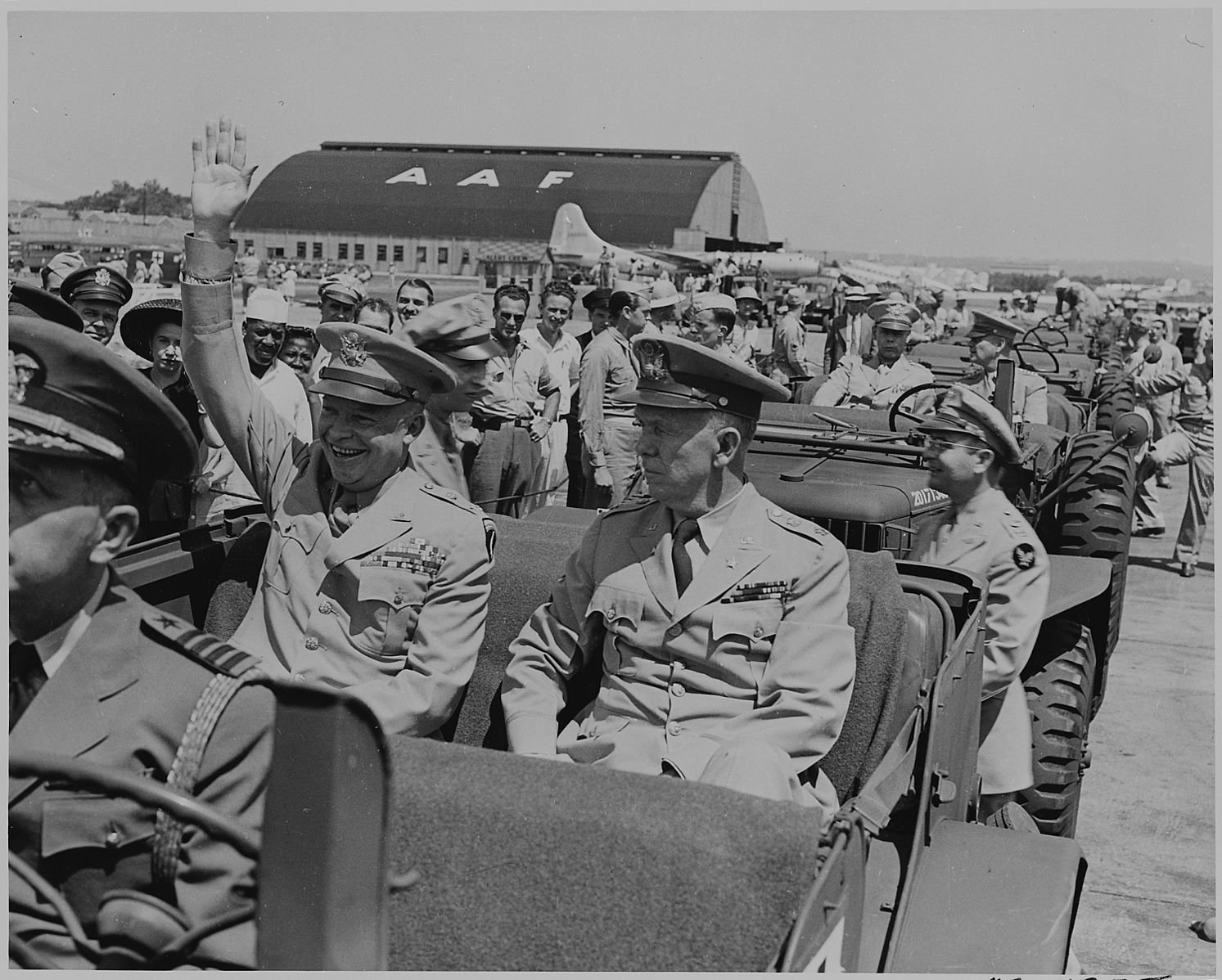 Photograph of General Dwight D. Eisenhower sitting in the back of a jeep with General George C. Marshall, waving to spectators at the airport in Washington.