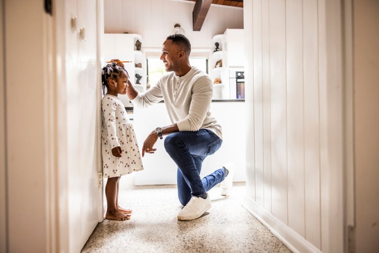 Father measuring daughter's height on wall in kitchen